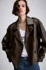 Cazadora de Zara Woman Collection confeccionada en material efecto piel color marrón oscuro. Presenta cuello con solapas, cierre frontal cruzado con botones, bolsillos delanteros y mangas largas con trabillas y hebillas ajustables en los puños.