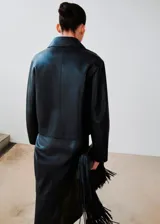 Chaqueta de cuero sintético negro con solapas clásicas, cierre frontal de botones ocultos y mangas largas amplias.
