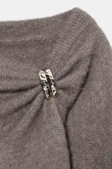 Jersey de punto color marrón topo, con cuello drapeado decorado con un broche metálico dorado y mangas largas de corte holgado.