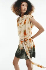 Vestido corto sin mangas de cuello redondo, con estampado tie-dye en tonos beige, naranja y verde oscuro. Presenta un lazo para atar en la cintura y cierre trasero con cremallera oculta.