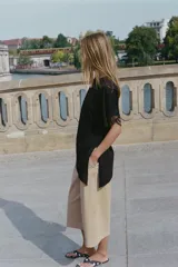 Camiseta negra de algodón con cuello redondo, manga corta y detalle de aplicación de encaje a tono en los puños. Presenta un diseño con bajo asimétrico y frunce lateral.