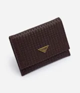 Billetera pequeña tipo sobre color marrón, marca Satínato, confeccionada en poliuretano con efecto trenzado. Cuenta con cierre de botón a presión y una placa metálica triangular con el logo de la marca en la solapa frontal.