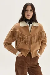 Bomber de tejido de punto color camel, con cuello de lana merino, cierre frontal, flecos decorativos en el frente y la espalda, y detalle de trenzas en las mangas.