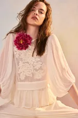 Camisa blanca de manga larga abullonada, con cuerpo de red transparente con bordados florales en tono crudo y aplique de flor grande fucsia en el hombro.