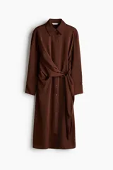 Vestido midi camisero de sarga liviana con brillo satinado, color marrón, de manga larga, con hombros caídos, botonadura frontal y puños sencillos. Presenta paneles drapeados cruzados en la cintura con tiras para atar al costado.