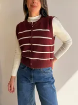 Chaleco de tejido de punto con diseño de rayas horizontales en color bordó y blanco. Presenta cuello redondo, cierre frontal con botones y terminaciones acanaladas en cuello, sisas y ruedo.