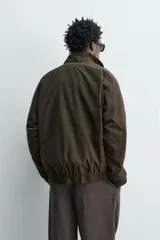 Cazadora bomber de corte relajado confeccionada en tejido técnico color negro. Presenta cuello subido, manga larga amplia, bolsillos de vivo en cadera, acabados elásticos y cierre frontal con cremallera de doble dirección.