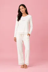 Pijama de descanso de dos piezas color crema, confeccionado en algodón con elastano. Incluye una remera de manga larga con bordado delicado en el pecho y terminación de encaje, y un pantalón largo con elástico en la cintura, bolsillos laterales y detalles de encaje en los bajos.