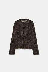 Blusa de manga larga con cuello redondo, confeccionada en tejido semitransparente con estampado paisley en tonos marrones oscuros. Presenta detalles de volantes y apliques de terciopelo en el frente y hombros, con cierre frontal de botones forrados.