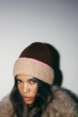 Gorro tipo beanie de punto, con diseño bicolor que combina marrón oscuro en la parte superior y beige en el borde, con una franja delgada en color rosado que separa ambos tonos.