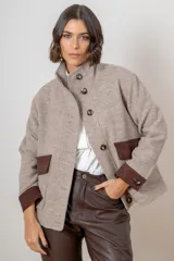 Campera de paño de lana color beige, con diseño oversize, cuello alto y cierre frontal de botones. Presenta detalles en pana color marrón en los puños y en las tapas de los bolsillos frontales.