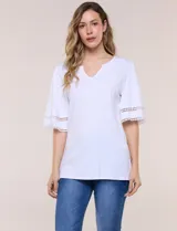 Remera blanca de silueta recta y algodón suave, con escote redondo y pequeña abertura central tipo gota. Presenta mangas de largo intermedio con aplicación horizontal de puntilla calada al tono y ruedo recto con tajos laterales.