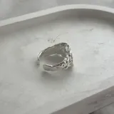 Anillo plateado con diseño irregular y abertura ajustable.
