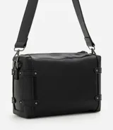 Cartera tipo shoulder de tamaño mediano, confeccionada en poliuretano con diseño rectangular. Presenta correas laterales decorativas con remaches metálicos, cierre superior con cremallera, herrajes en acabado gunmetal y correa larga ancha ajustable.