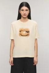 Remera oversize de jersey de algodón color beige claro, con cuello redondo, mangas cortas y estampa frontal de unos labios con un caramelo.