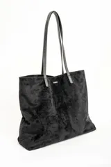 Bolso tipo tote de gran tamaño en color bordó, confeccionado en material con textura similar a la gamuza. Cuenta con doble asa larga para llevar al hombro y una pequeña placa metálica decorativa en el frente.