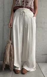 Pantalón palazo de lino color beige, de calce amplio y fluido, con tablas en el frente, botón, cierre y cordón ajustable en la cintura.
