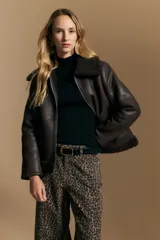 Campera tipo gamulán de cuero sintético negro, con interior y detalles de corderito sintético al tono en cuello y ruedo. Presenta cierre frontal metálico y diseño de silueta relajada.