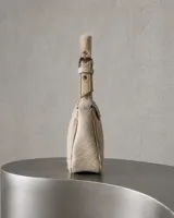 Cartera de mano de cuero vacuno con pelo largo en tono crudo y vainilla, con forma curva y solapa frontal con cierre magnético y aplique metálico con monograma. Cuenta con una correa ajustable corta para llevar al hombro o en la mano.