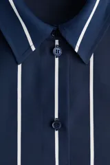 Camisa de manga larga con cuello clásico, cierre frontal abotonado y puños con botón. Presenta un diseño de rayas verticales blancas sobre fondo azul marino, con bajo redondeado.