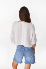 Camisa de lino azul marino, de corte crop y holgado, con cuello redondo, botonadura frontal y mangas amplias con vuelta.