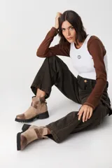 Bota corta de cuero color chocolate, con puntera reforzada en cuero liso y cuerpo en gamuza. Presenta una tira decorativa con hebilla metálica dorada en el tobillo y suela de goma tipo tractor.