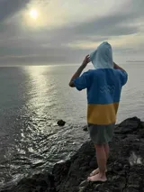 Poncho corto azul con franja horizontal amarilla y bolsillo estampado con motivos florales.