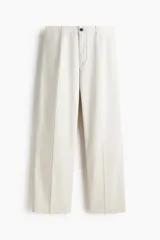 Pantalón sastrero de corte relajado en sarga color beige, con cierre y botón, bolsillos laterales y bolsillos traseros con botón oculto. Presenta piernas con pliegues.