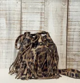 Mini cartera tipo bucket con diseño de estampado animal print, confeccionada en cuero con flecos decorativos en todo el frente. Cuenta con cierre de cordón ajustable, herrajes metálicos en tono bronce y correa larga regulable.