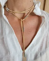 Collar estilo corbatín confeccionado en tiento de cuero color suela, con detalle de cuentas metálicas plateadas distribuidas a lo largo de las tiras.