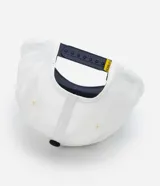 Gorra blanca de sarga con visera azul marino y bordado de Snoopy jugando baseball.