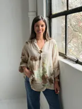 Blusa beige de lino con estampado floral en tonos marrones y verdes, escote en V con botón dorado decorativo y mangas largas.