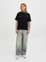 Remera negra de manga corta y cuello redondo, con un estampado gráfico en la espalda que muestra una escena urbana con edificios y texto que incluye "Metropolitan Scenes 1990" y el logo "JACK&JONES WORLDWIDE".