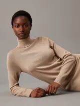 Vestido color beige de lana merino, corte recto, largo hasta la rodilla, cuello alto y mangas largas.