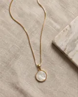 Collar de acero con baño de oro y cadena fina de eslabones, con un dije circular dorado que presenta una imagen en relieve de la Virgen sobre fondo de nácar.