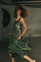 Falda midi de tiro medio color verde oscuro, confeccionada en tejido satinado con volantes en cascada y cierre lateral con cremallera oculta.
