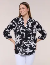 Blusa de gasa de calce suelto y caída ligera, color azul con estampado floral blanco. Presenta escote en V con cuello mao, tabla central, mangas largas regulables con presilla y botón, ruedo redondeado de estilo mullet y espalda con canesú y pliegue central.