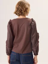 Camisa de color marrón con diseño combinado, presentando mangas abullonadas con volados en los hombros y cuerpo de algodón. Combina una textura de tela de camisa en mangas y delantero con una espalda de tejido elástico.