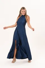 Vestido largo azul de tafeta con textura corrugada, cuello halter, espalda descubierta y falda amplia con tajo lateral y volados.