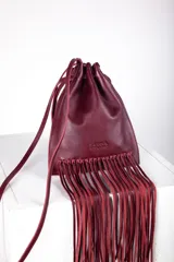 Cartera tipo saco color bordó, confeccionada en cuero, con cierre de cordón ajustable y flecos largos en la parte inferior. Incluye correa de hombro fina.