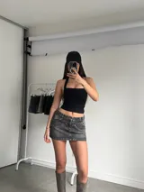 Minifalda de jean rígido color negro con efecto lavado acid wash, tiro bajo y diseño de bolsillos delanteros superpuestos con detalles de tachas metálicas.