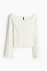 Top corto de punto acanalado color blanco, con escote amplio que deja los hombros al descubierto y leve escote en V. Mangas largas acampanadas con ribete de volados en puños y bajo.