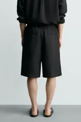 Bermuda relaxed fit de color negro, confeccionada en tejido fluido con viscosa y modal. Presenta cintura elástica ajustable con cordón, pliegues en el delantero, bolsillos frontales y bolsillos traseros de vivo.