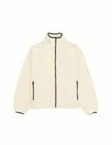 Campera de tejido tipo teddy color crema, con cierre frontal completo, cuello alto y bolsillos laterales con cierre. Presenta detalles de ribetes en color negro en el cuello, puños y cierres.