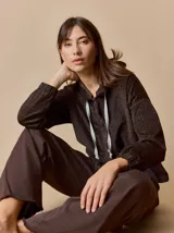 Campera de corte holgado con textura aterciopelada y estampado de cuadros sutil. Presenta cuello con cordones ajustables, cierre frontal con botones y mangas largas con puños elásticos.