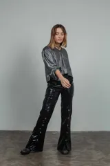 Pantalón negro de cuero sintético con corte acampanado, tiro alto y cierre con botones a presión en los laterales.