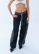 Pantalon deportivo de estilo urbano, confeccionado en tela técnica, con cintura elástica ajustable mediante cordón. Presenta un diseño bicolor en negro y gris oscuro con líneas laterales en contraste.