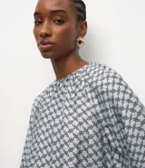 Blusa de mangas largas abullonadas con cuello redondo fruncido y diseño de estampa geométrica en tonos azul y blanco.