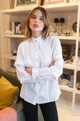 Camisa blanca de algodón con cuello alto tipo mao con volados, cierre frontal de botones y mangas largas con detalles de volados horizontales y puños con volados.