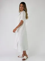 Vestido largo holgado color gris, con mangas cortas, escote en V y detalles de flecos en los bordes y aberturas laterales.